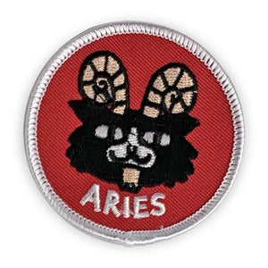 A circular embroidered patch. A ram with a cat's face is the focus. It is black with white details, and gold horns. It sit above the word "Aries" in white. The patch is red with a white border. 