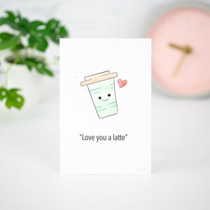 A white flat card that says "Love you a latte" with a cute cartoon style illustration of a travel mug with a smiley face and heart